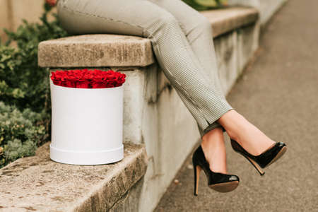 Image of woman's legs wearing black high heel shoes and checked trousers next to white box with red...