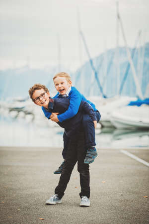 Two funny brothers playing together outside, elder brother caring younger  one on his backの写真素材