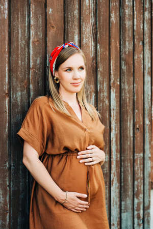 Outdoor portrait of stylish pregnant woman, wearing brown dress and stylish headbandの写真素材