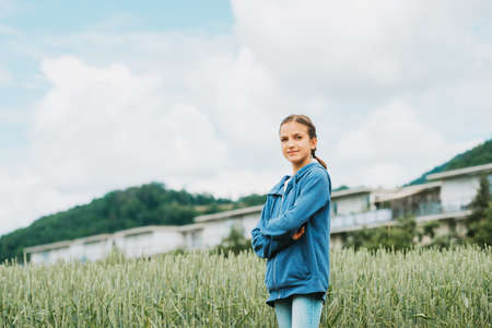 Outdoor portrait of happy young girl with braids, smiling kid posing outside, wearing blue zip hoody