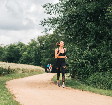 Portrait of young beautiful fit woman jogging in nature, wearing black activewear, athlete model...
