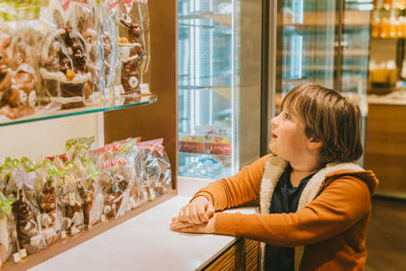 Funny kid boy admiring easter chocolate bunnies in chocolate shopの写真素材