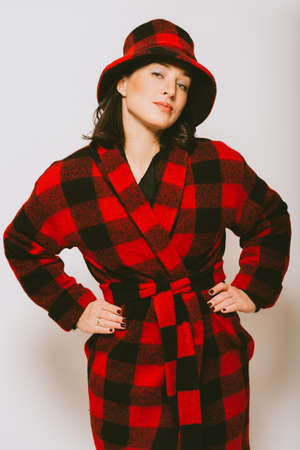 Studio portrait of beautiful woman wearing checked red and black coat and a hat, posing on white backgroundの写真素材