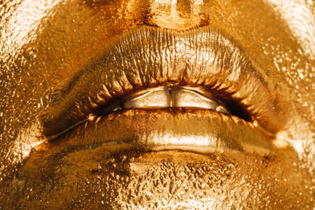 Close up image of woman lips, face covered with bright golden paint, makeup and beauty conceptの写真素材