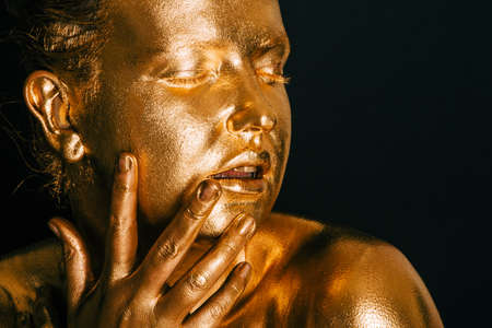Portrait of sensual woman covered with golden paint, posing on black background, eyes closedの写真素材