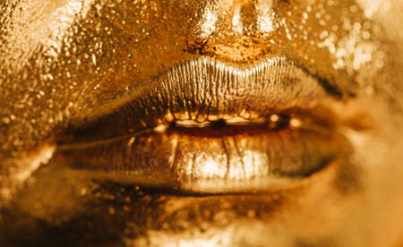 Close up image of woman lips, face covered with bright golden paint, makeup and beauty conceptの写真素材