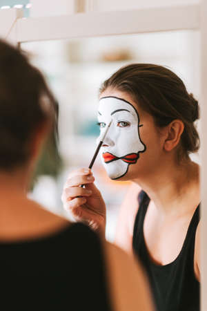 Woman actress looking in the mirror and doing mime makeup