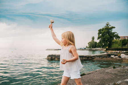 Outdoor portrait of pretty young girl playing by the lake, throwing stones into water