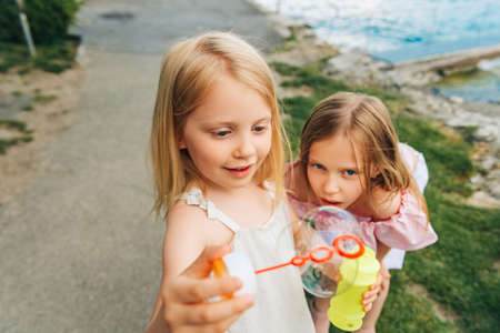 Two funny girls playing with soap bubbles outside, children having fun togetherの写真素材