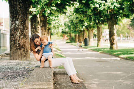 Happy mother spending time with children in summer park, playing with babyの写真素材