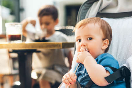 Outdoor portrait of happy baby boy playing with a spoon, sitting in a buggy