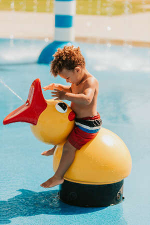 Adorable african baby boy playing on water playground on a hot summer day