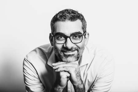Black and white portrait of handsome man wearing blue shirt and glasses, leaning on hands, posing on white backgroundの写真素材