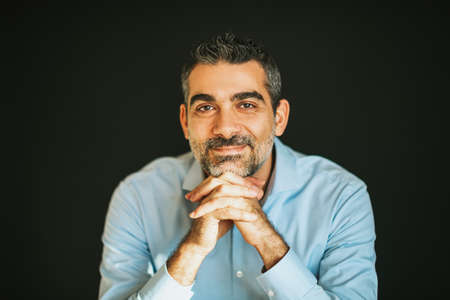 Portrait of handsome man wearing blue shirt, leaning on hands, posing on black background