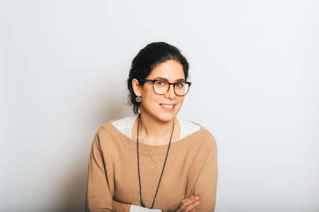 Studio portrait of beautiful brunette woman, wearing glasses, arms crossed, posing on white backgroundの写真素材