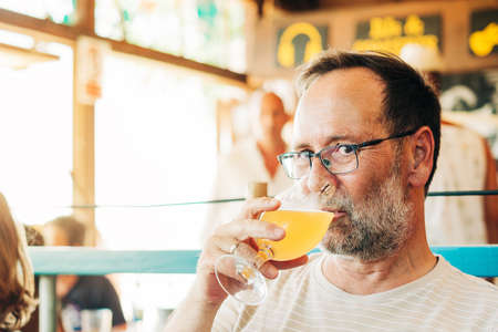 Middle age man drinking beer in summer bar, wearing glasses