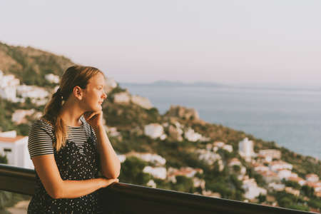 Young girl admiring beautiful landscape from the balcony, summer vacation by the sea, family travel with childrenの写真素材