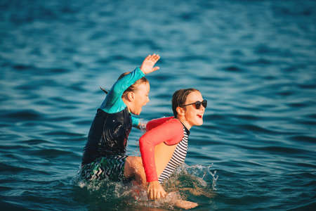 Two funny kids, little boy and teenage girl playing together in the sea, wearing sunsafe swimming suits, summer vacation with childrenの写真素材