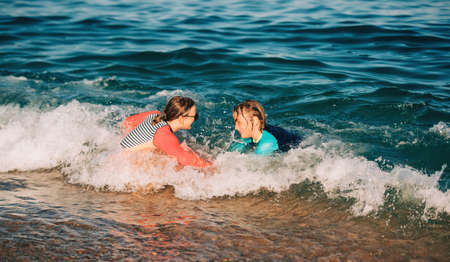 Two funny kids, little boy and teenage girl playing together in the sea, wearing sunsafe swimming...