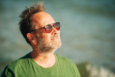 Outdoor portrait of happy middle age man enjoying nice sunny day on the beach, wearing green t-shirt...