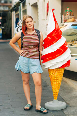 Outdoor portrait of pretty teenage girl with red dyed hair posing outside with giant ice creamの写真素材