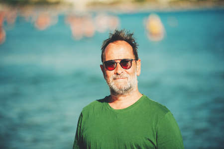 Outdoor portrait of happy middle age man enjoying nice sunny day on the beach, wearing green t-shirt...