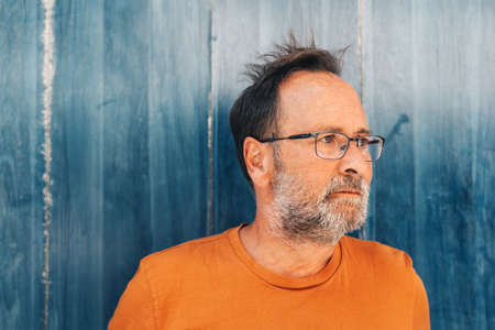 Outdoor summer portrait of middle age man, wearing orange t-shirt and eyeglasses, posing on blue...