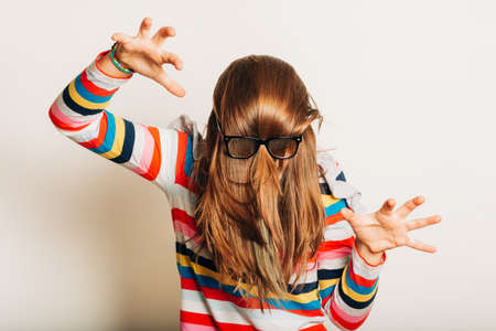 Studio portrait of young girl fooling around, hiding behind, hair, acting silly, time for haircut, hair completely covering the face with glasses overの写真素材