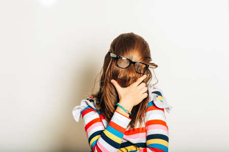 Studio portrait of young girl fooling around, hiding behind, hair, acting silly, time for haircut,...