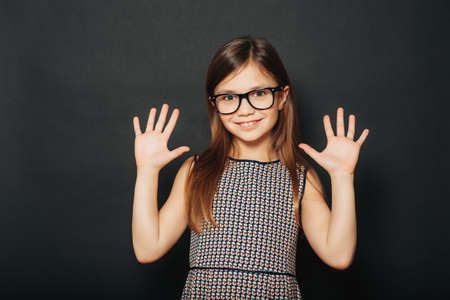 Studio portrait of pretty little girl, wearing eyeglasses, posing on black background