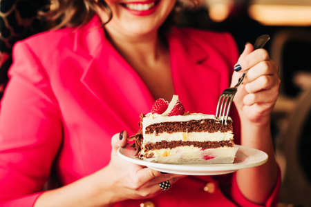 Close up image of woman eating cake Black Forest decorated with white chocolate and raspeberries
