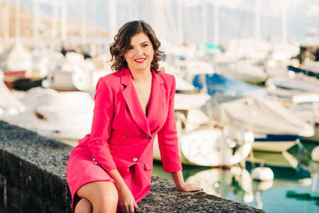 Outdoor fashion portrait of young stylish woman, resting by the lake, wearing pink jacket dress の写真素材