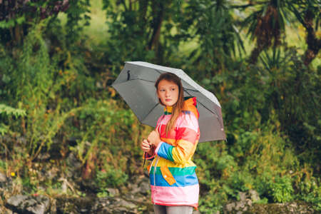 Outdoor portrait of young girl under the rain, holding umbrella, wearing colorful rain jacketの写真素材