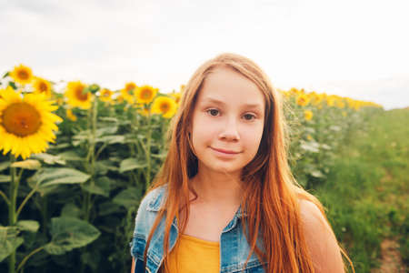 Outdoor portrait of cute young red-haired girl posing in sunflower fieldの写真素材