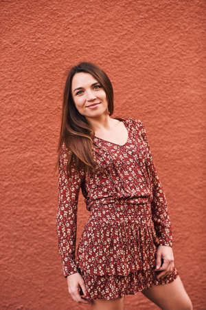 Outdoor portrait of pretty young woman with long straight brown hair, posing on terracotta color...