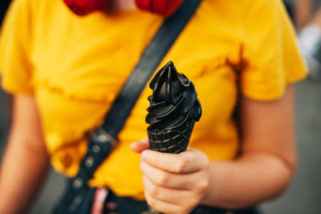 Young teen girl holding black ice cream, street food festival 