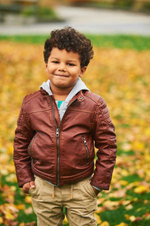 Outdoor autumn portrait of cute african boy, wearing brown leather jacket, child having fun in parkの写真素材