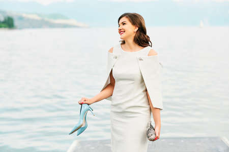 Outdoor fashion portrait of beautiful stylish woman wearing white dress, resting by the seaの写真素材