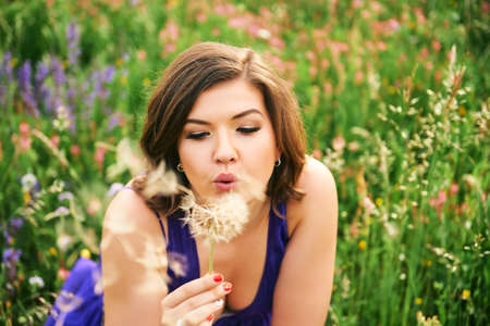 Summer portrait of happy young woman relaxing in wild flower field, playing with dandelionの写真素材