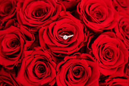 Beautiful bouquet of bright red roses with diamond engagement ring, top viewの写真素材