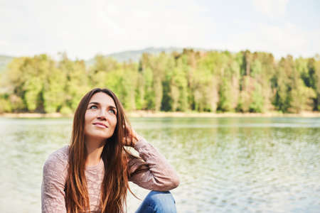 Outdoor portrait of young beautiful woman relaxing by river on a nice warm dayの写真素材