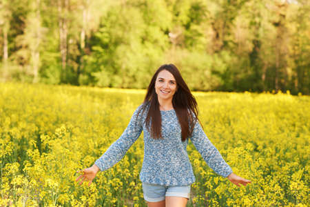 Spring portrait of happy young woman posing in colza field