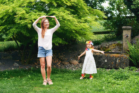 Young mother dancing with cute little daughter in garden, family spending time togetherの写真素材