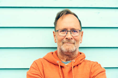 Outdoor portrait of handsome middle age man posing against turquoise background, wearing bright orange hoody and eyeglassesの写真素材