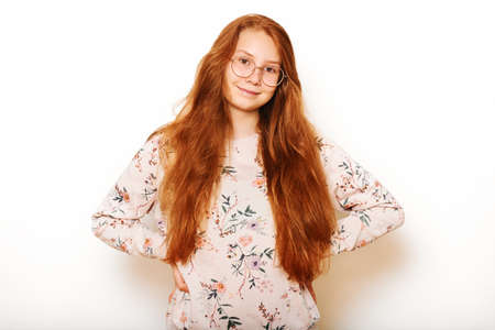 Studio portrait of pretty young teen girl with long red hair, posing on white backgroundの写真素材