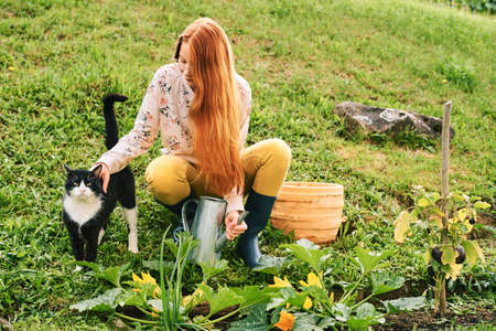 Young teen girl working in a garden, playing with a cat