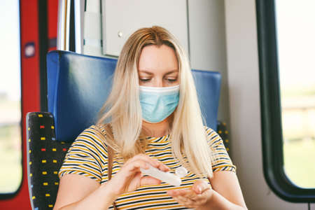 Middle age woman on the train, wearing face mask, disinfect hands with a sanitizer