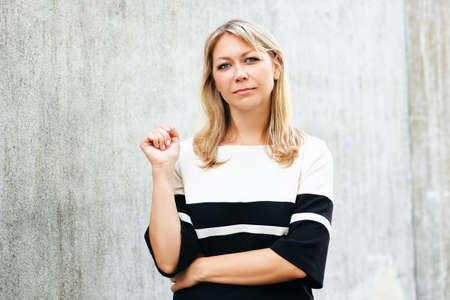 Outdoor portrait of middle age woman, leaning on grey wall