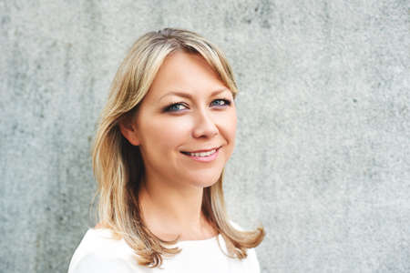 Outdoor close up portrait of middle age woman posing next to grey backgroundの写真素材