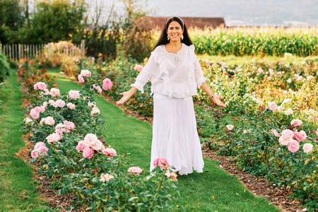 Woman enjoying nice day in beautiful rose garden, wearing white clothesの写真素材